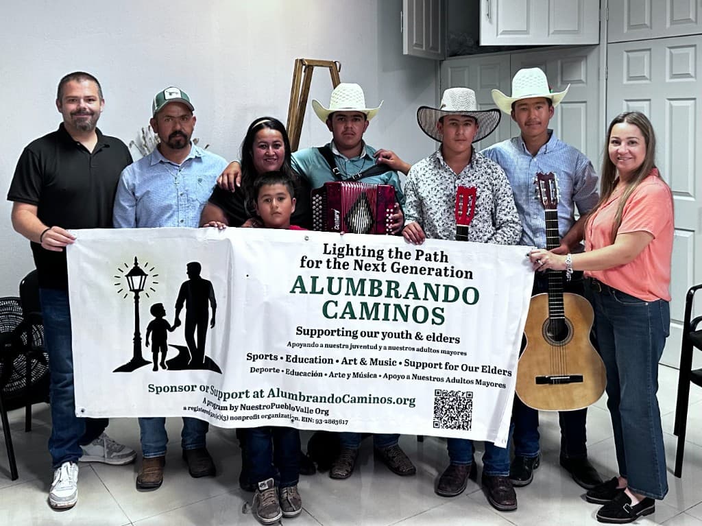 Community members and youth with the Alumbrando Caminos banner — a Nuestro Pueblo Valle program supporting youth, elders, sports, education, and the arts.